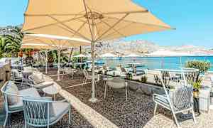 En terrasse med sitteplasser og parasoller ved sjøen. (AI-generert tekst)