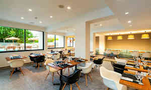 En moderne restaurant med tremøbler, vinduer med utsikt mot en uteservering og flere borddekninger. (AI-generert tekst)