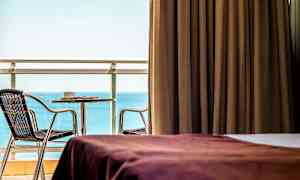 Rom med brun gardin, utsikt over havet og møblert balkong. (AI-generert tekst)