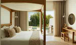 Et soverom med en himmelseng, utsikt mot en terrasse og bassengområde. (AI-generert tekst)