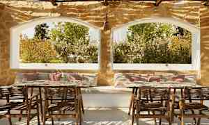 En uteplass med sitteplasser og bord, steinmur og store vinduer med utsikt over grøntområder. (AI-generert tekst)