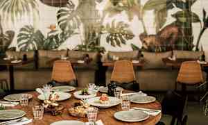 Et dekket trebord omgitt av stoler, med en bakgrunn av veggmalerier med plantemotiver. (AI-generert tekst)