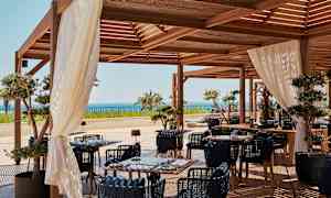 Uteservering med tremøbler, hvite gardiner og havutsikt. (AI-generert tekst)