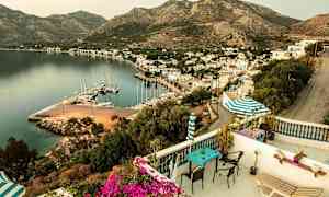 Utsikt fra terrassen over en havn med båter, omkringliggende bygninger og fjell i bakgrunnen. (AI-generert tekst)