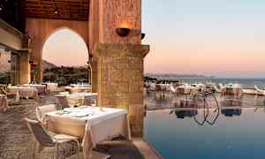 Utendørs spiseområde med dekkede bord ved siden av et basseng og havutsikt ved solnedgang. (AI-generert tekst)