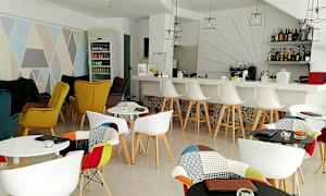 Innendørs bilde av en elegant kafé med fargerike stoler, et barområde og dekorative elementer. (AI-generert tekst)