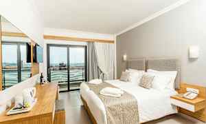 Et hotellrom med en stor seng, lyse møbler og en balkong med utsikt. (AI-generert tekst)