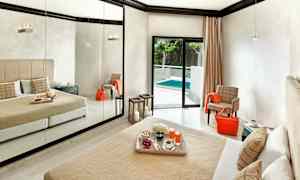 Et hotellrom med en stor speilvegg, en seng med beige sengeteppe og puter, og en balkongdør som fører ut til et basseng. (AI-generert tekst)