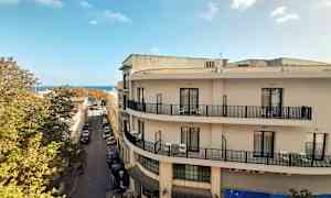 Utsikt over en gate med bygninger, en blå himmel kan sees i bakgrunnen. (AI-generert tekst)