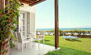 En uteplass med bord og stoler samt solsenger på plen nær havet. (AI-generert tekst)