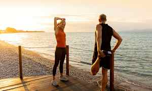 To personer strekker ut på en trebrygge ved en strand ved solnedgang. (AI-generert tekst)