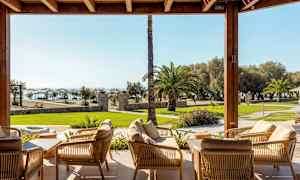 Avslapningsområde med sittemøbler som leder til en hage med palmer og havutsikt. (AI-generert tekst)