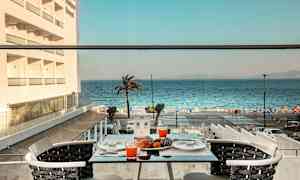 Utsikt fra et bord på en terrasse med appelsinjuice og bakverk, mot havet og en palme. (AI-generert tekst)