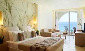 Hotellrom med havutsikt og moderne innredning inkludert seng, sofa og balkong. (AI-generert tekst)