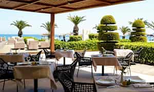 Uteservering med dekte bord, palmer og utsikt mot havet. (AI-generert tekst)