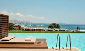 Utsikt fra et basseng mot havet, solsenger og parasoller. (AI-generert tekst)