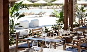 Utemøbler med mat og drikke servert, bassengområde i bakgrunnen. (AI-generert tekst)