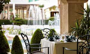 En oppdekket spiseplass utendørs med utsikt over en hage med fontener. (AI-generert tekst)