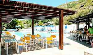 Utendørs bassengområde med solsenger, parasoller, bord og stoler under skyggefulle tak. (AI-generert tekst)