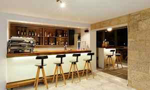 En moderne bardisk med høye stoler, flasker på hyller og lys belysning. (AI-generert tekst)