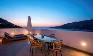 Terrasse med bord, stoler og solsenger ved solnedgang. (AI-generert tekst)