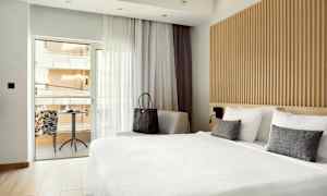 Bilde av et hotellrom med stor seng og sittegruppe ved vinduet som fører ut til balkongen. (AI-generert tekst)