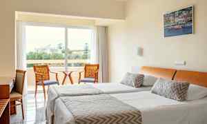 Et hotellrom med to enkeltsenger, en sittegruppe og utsikt til grønne omgivelser. (AI-generert tekst)