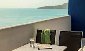 To stoler med et grønt teppe på den ene, stående ved et bord som har et vannglass og en avis, med havutsikt. (AI-generert tekst)