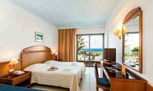 Et hotellrom med to senger, et skrivebord, et speil og en balkong med utsikt over havet. (AI-generert tekst)