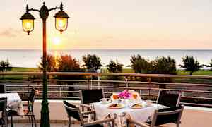 Utsikt over et bord med frokostservering på en terrasse med havet i bakgrunnen. (AI-generert tekst)