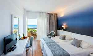 Hotellrom med to senger og balkong med utsikt over havet. (AI-generert tekst)