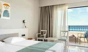 Hotellrom med dobbeltseng, to stoler og et bord ved vindu med havutsikt. (AI-generert tekst)