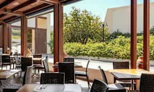 En utendørs terrasse med bord og stoler, omgitt av grøntområder. (AI-generert tekst)