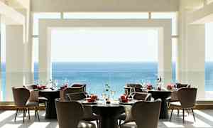 En moderne restaurant med utsikt over havet, møblert med runde bord og komfortable stoler. (AI-generert tekst)