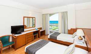 Hotellrom med to enkeltsenger, skrivebord, stol og havutsikt. (AI-generert tekst)