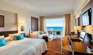 Hotellrom med dobbelseng, sittegruppe og utsikt mot havet. (AI-generert tekst)