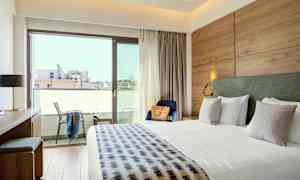 Et hotellrom med en stor seng, skrivebord, stol og balkong. (AI-generert tekst)