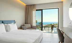 Hotellrom med seng, sofa og utsikt over havet. (AI-generert tekst)