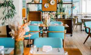 Et moderne innredet restaurantområde med bord, turkise stoler og dekorative planter. (AI-generert tekst)