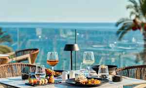 Et dekket bord med mat og drikke på en terrasse med utsikt over havet. (AI-generert tekst)