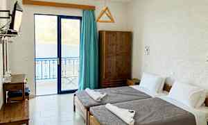 Et hotellrom med to enkeltsenger og utsikt over havet gjennom glassdører. (AI-generert tekst)