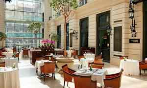 En lys restaurant med bord, stoler og planter i et glassinnelukket miljø. (AI-generert tekst)