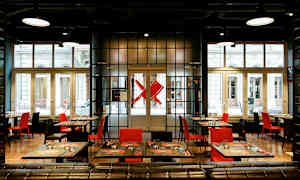 Moderne restaurant med røde og svarte stoler samt dekkede bord foran store vinduer. (AI-generert tekst)