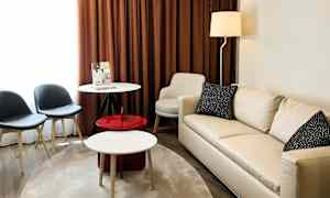 Et stue med en lys sofa, et rundt bord, to stoler og brune gardiner. (AI-generert tekst)