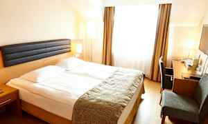 Hotellrom med en dobbeltseng, et skrivebord og en stol. Rommet har store vinduer med gardiner. (AI-generert tekst)