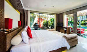 Et hotellrom med en stor seng med hvitt sengetøy og røde puter foran et stort vindu som vender ut mot en hage. (AI-generert tekst)