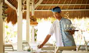 En servitør med et serveringsbrett og glass forbereder et bord på en restaurant. (AI-generert tekst)