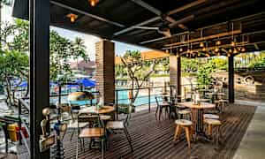 En uteservering med bord og stoler, samt et basseng i bakgrunnen. (AI-generert tekst)