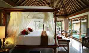 Et soverom med en himmelseng, hvite gardiner og røde puter. Gulv-til-tak-vinduer slipper dagslyset inn i rommet, med utsikt over et lite basseng og grønn vegetasjon. (AI-generert tekst)