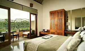 Et soverom med en seng oppredd med grønt og hvitt sengetøy. Rommet har et tre-garderobeskap, nattbord og en stor speil. Glassdører fører til en balkong med utsikt over frodig natur. (AI-generert tekst)